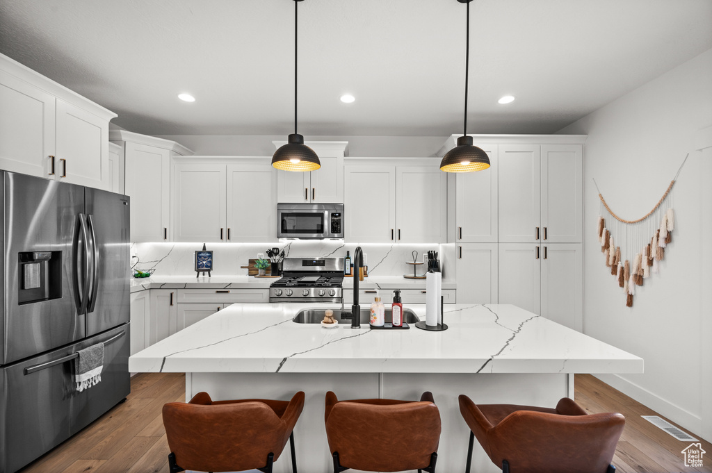 Kitchen featuring a center island with sink, appliances with stainless steel finishes, dark hardwood / wood-style flooring, and white cabinetry