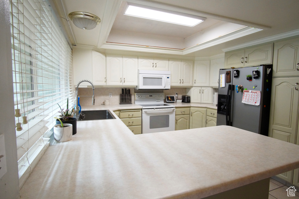Kitchen featuring a raised ceiling, tasteful backsplash, sink, white appliances, and kitchen peninsula