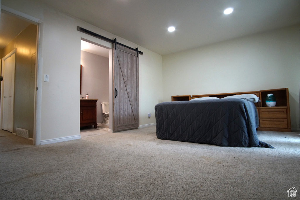 Bedroom with connected bathroom, light colored carpet, and a barn door