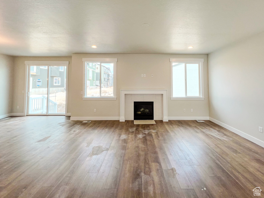Unfurnished living room featuring dark hardwood / wood-style flooring, a healthy amount of sunlight, and a brick fireplace