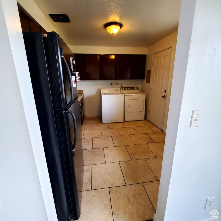 Kitchen with dark brown cabinetry, independent washer and dryer, light tile floors, and black refrigerator