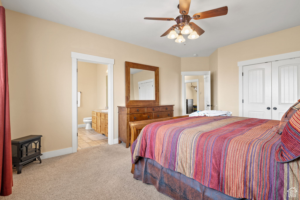 Bedroom featuring ensuite bath, a closet, light colored carpet, a wood stove, and ceiling fan