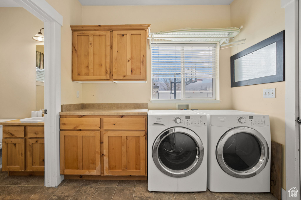 Washroom with washer hookup, washer and clothes dryer, dark tile floors, and cabinets