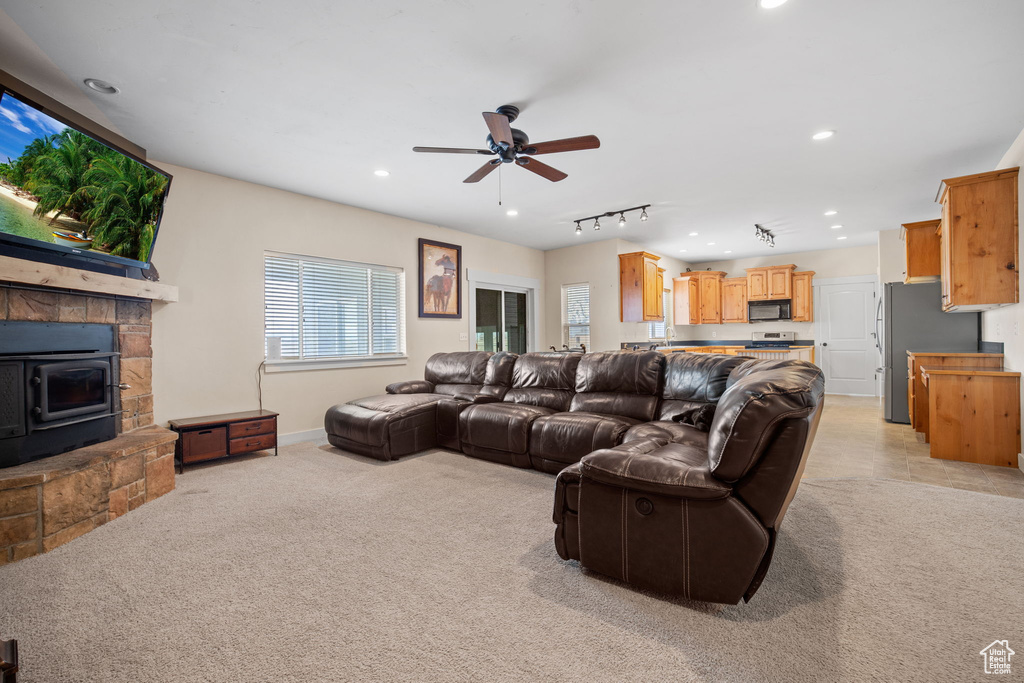 Carpeted living room with a stone fireplace, track lighting, and ceiling fan