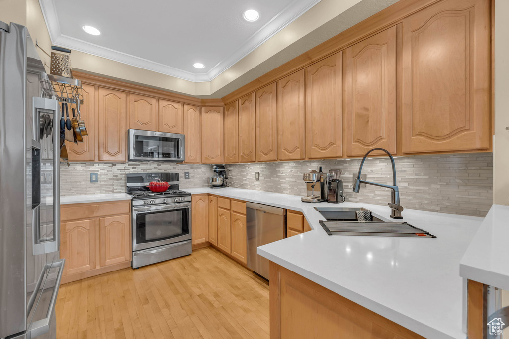Kitchen featuring ornamental molding, light brown cabinetry, backsplash, appliances with stainless steel finishes, and light hardwood / wood-style floors