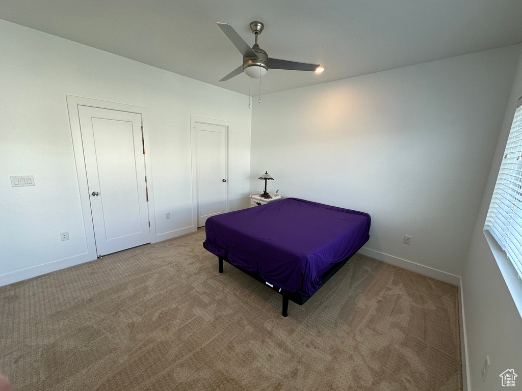 Bedroom with light colored carpet, multiple closets, and ceiling fan