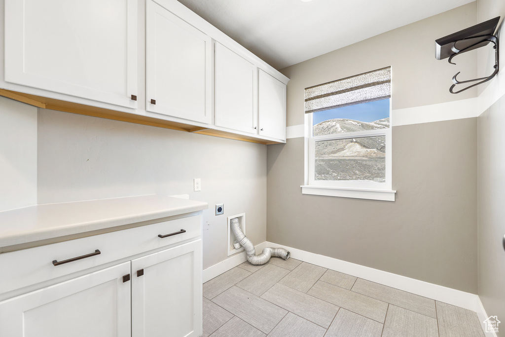 Laundry room featuring hookup for an electric dryer, light tile floors, and cabinets