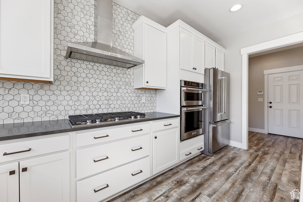 Kitchen with wall chimney range hood, hardwood / wood-style floors, appliances with stainless steel finishes, and backsplash