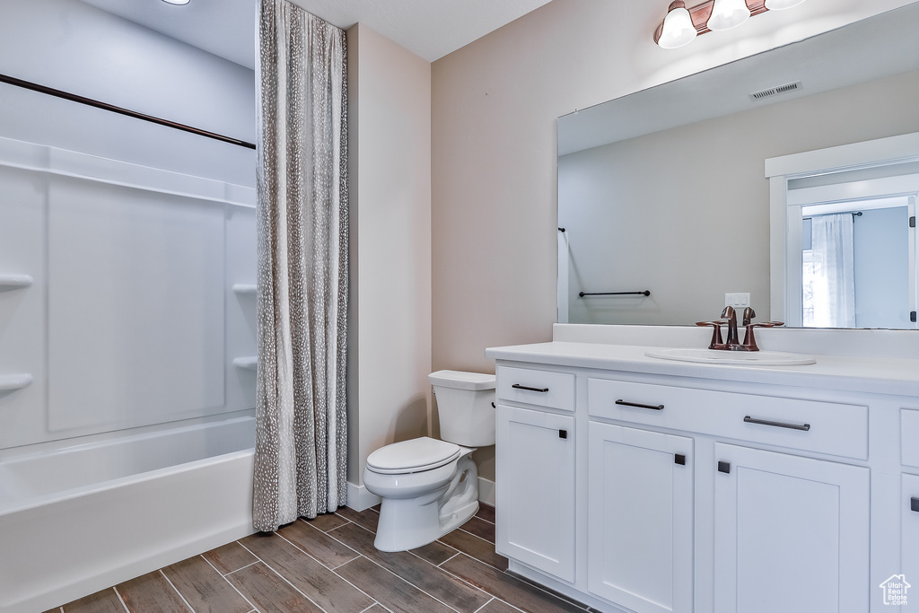Full bathroom with vanity, toilet, wood-type flooring, and shower / bathtub combination with curtain