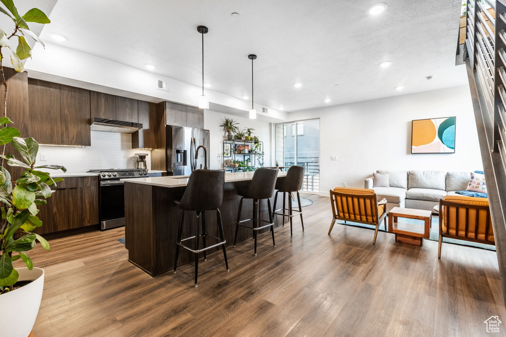 Kitchen with dark brown cabinets, light hardwood / wood-style flooring, stainless steel appliances, and an island with sink