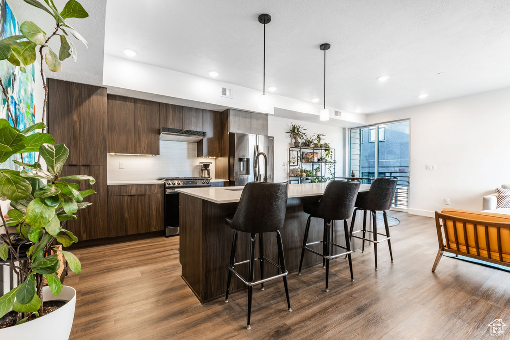 Kitchen with appliances with stainless steel finishes, a center island with sink, light hardwood / wood-style floors, a breakfast bar area, and dark brown cabinetry