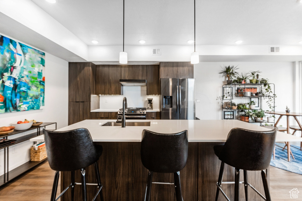 Kitchen with sink, hanging light fixtures, light hardwood / wood-style flooring, stainless steel appliances, and a breakfast bar area