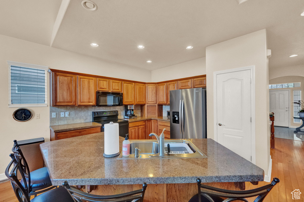 Kitchen with sink, light hardwood / wood-style floors, backsplash, black appliances, and a breakfast bar area
