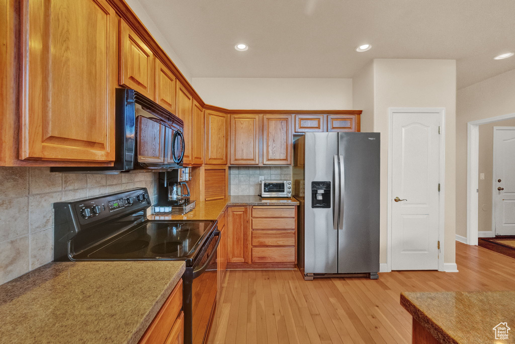 Kitchen featuring backsplash, black appliances, and light hardwood / wood-style flooring