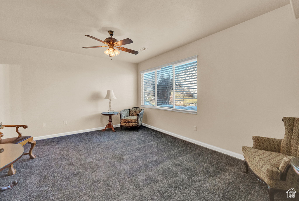 Living area with dark colored carpet and ceiling fan