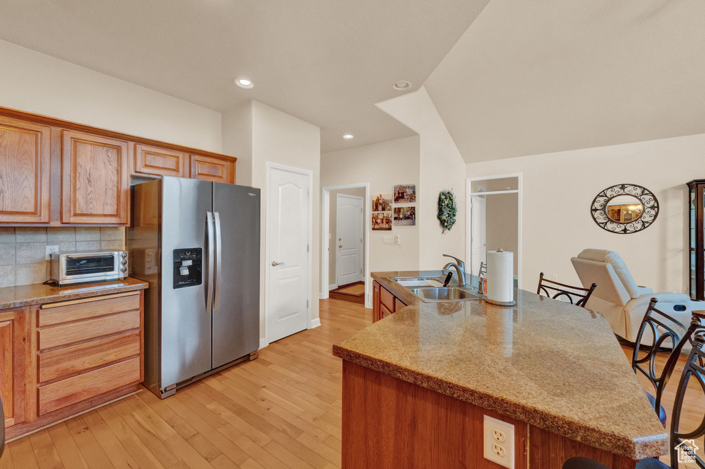 Kitchen featuring sink, vaulted ceiling, stainless steel refrigerator with ice dispenser, backsplash, and light wood-type flooring