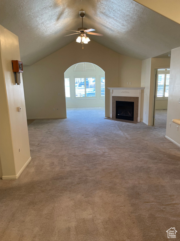 Unfurnished living room with light carpet, ceiling fan, a textured ceiling, and lofted ceiling