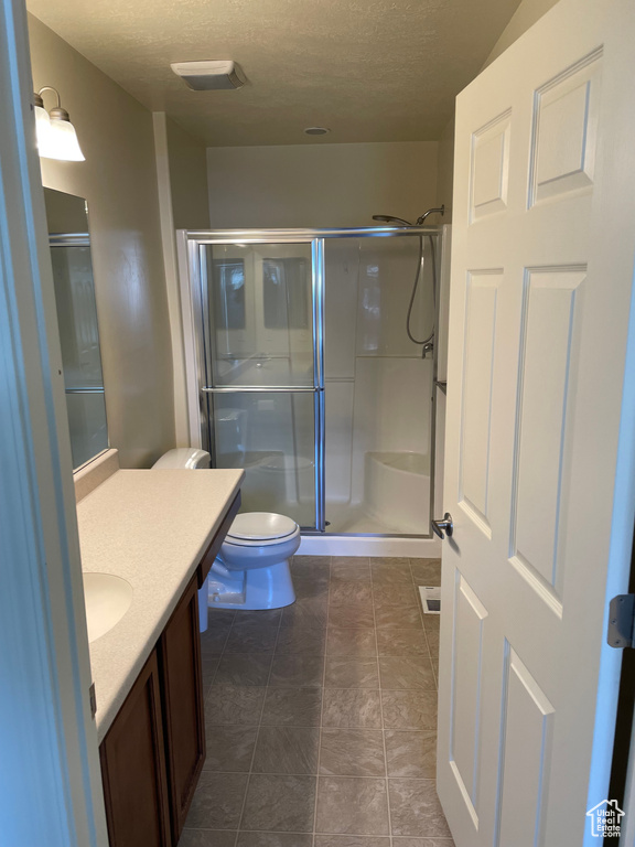 Bathroom with a textured ceiling, vanity, walk in shower, toilet, and tile floors