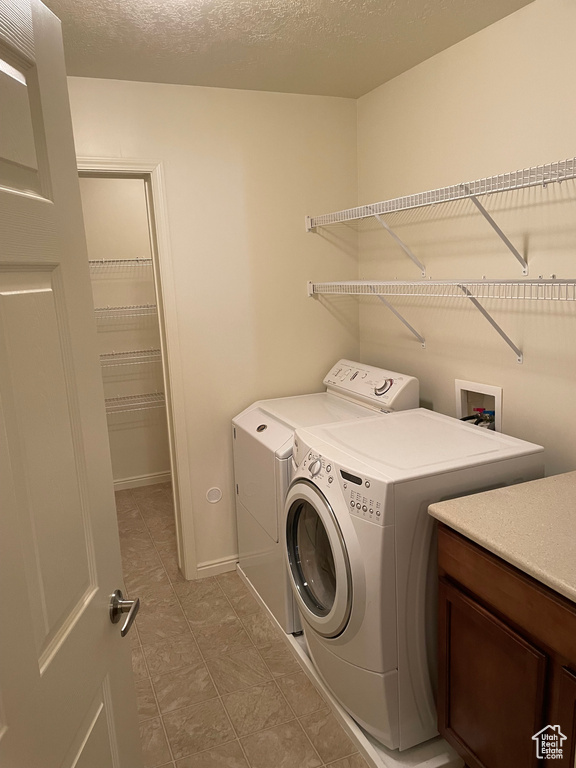 Clothes washing area featuring cabinets, washer hookup, light tile floors, and washing machine and clothes dryer