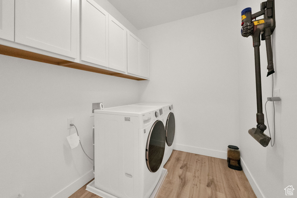 Clothes washing area with cabinets, light wood-type flooring, washing machine and dryer, and hookup for a washing machine