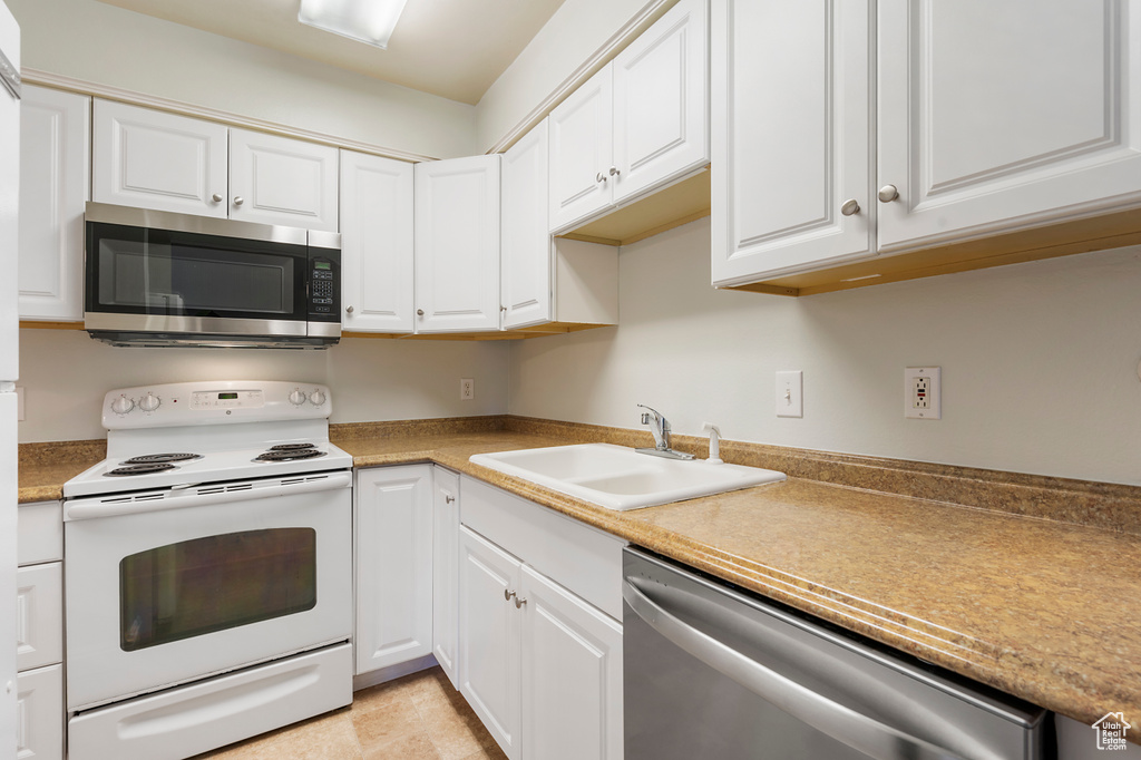 Kitchen with light tile flooring, white cabinets, appliances with stainless steel finishes, and sink