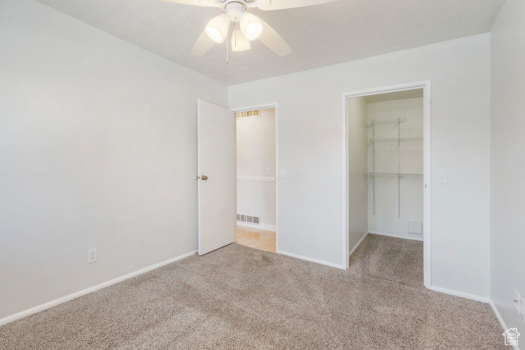 Unfurnished bedroom with a spacious closet, a closet, light carpet, and ceiling fan