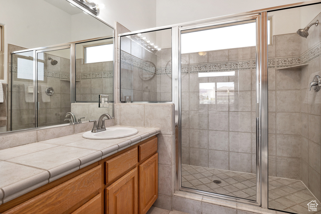 Bathroom with vanity with extensive cabinet space, tile flooring, tile walls, and an enclosed shower