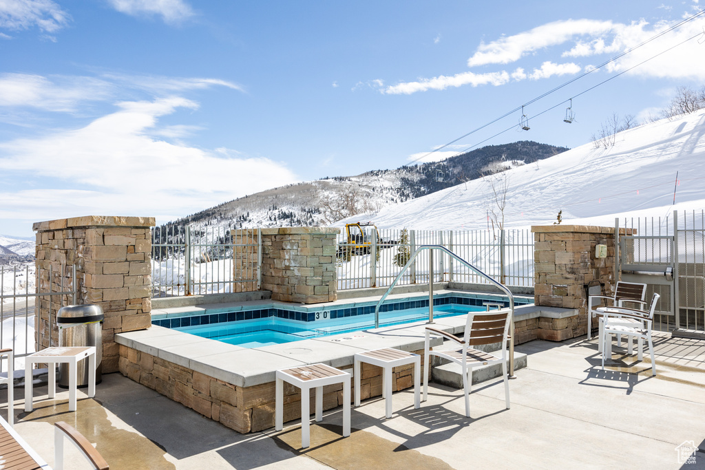 Snow covered pool with a patio area, an outdoor hot tub, a mountain view, and an outdoor fireplace