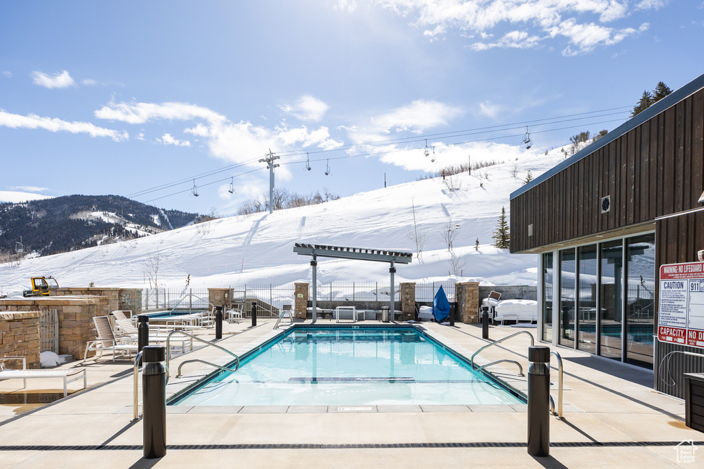 Snow covered pool featuring a patio area and a mountain view