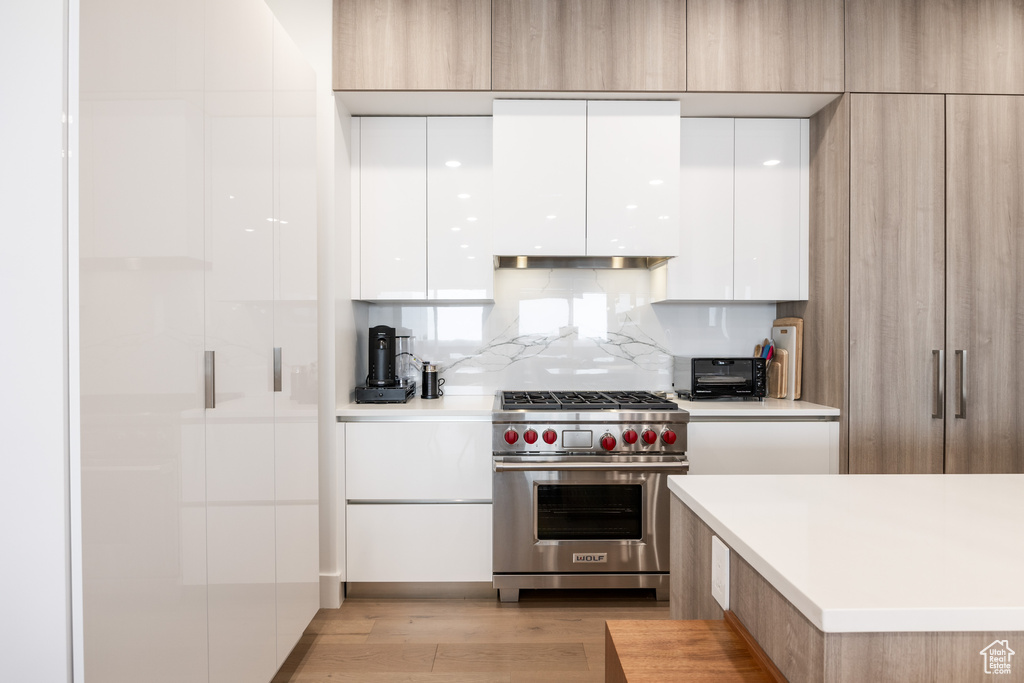 Kitchen with premium range, backsplash, white cabinets, and light hardwood / wood-style flooring