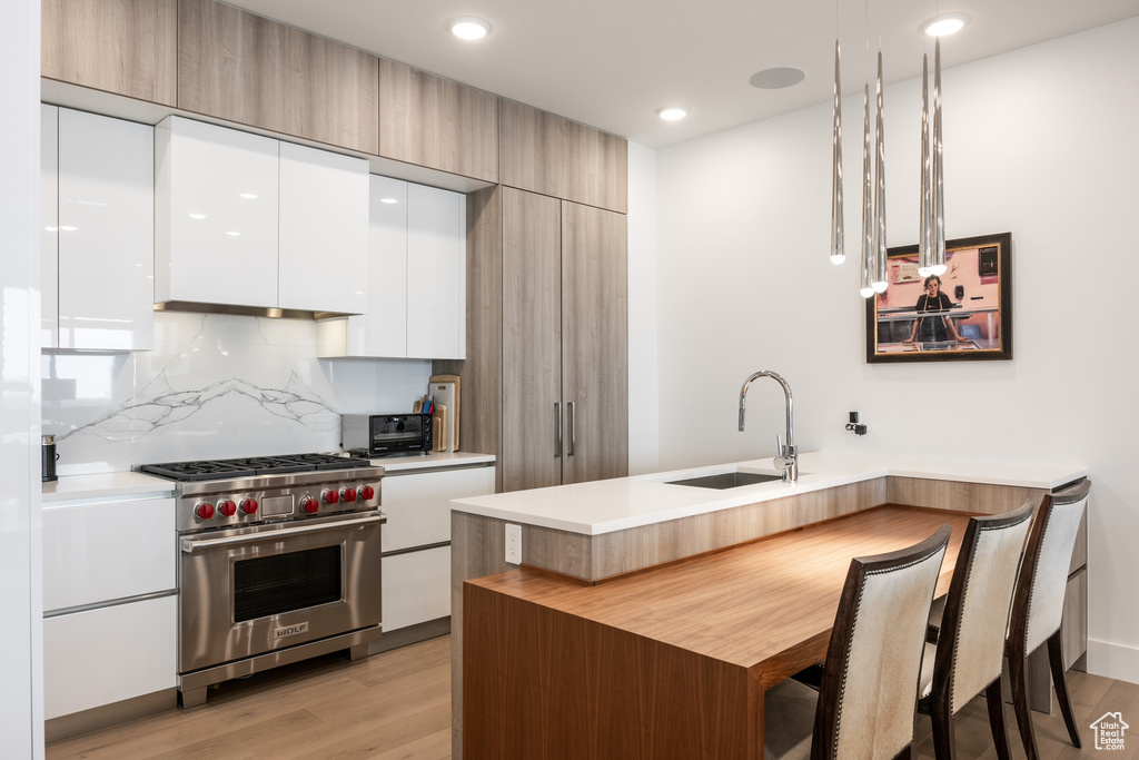Kitchen with white cabinetry, premium range, sink, pendant lighting, and light wood-type flooring