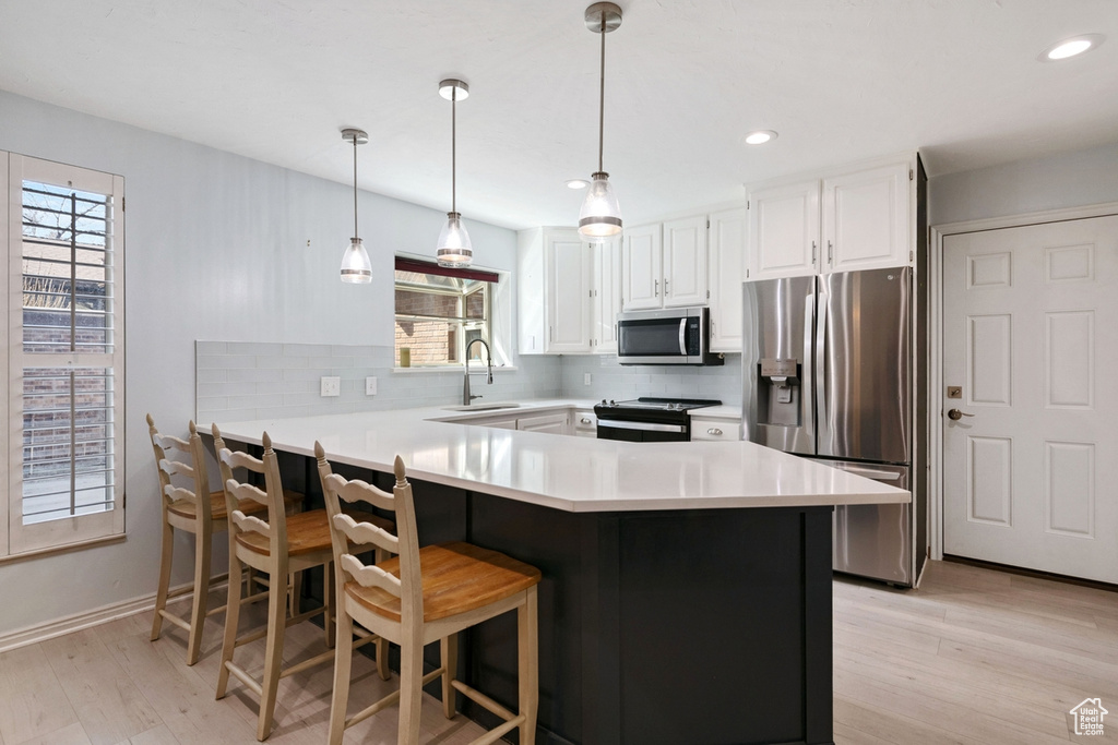 Kitchen featuring hanging light fixtures, appliances with stainless steel finishes, light wood-type flooring, and backsplash