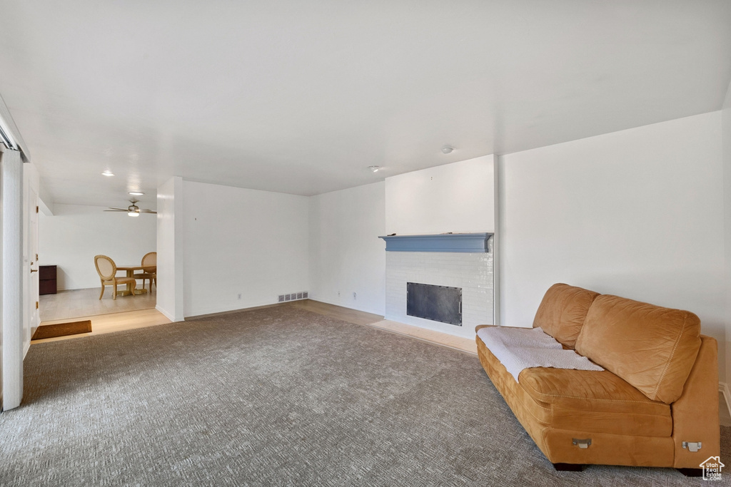 Unfurnished room with light carpet, ceiling fan, and a brick fireplace
