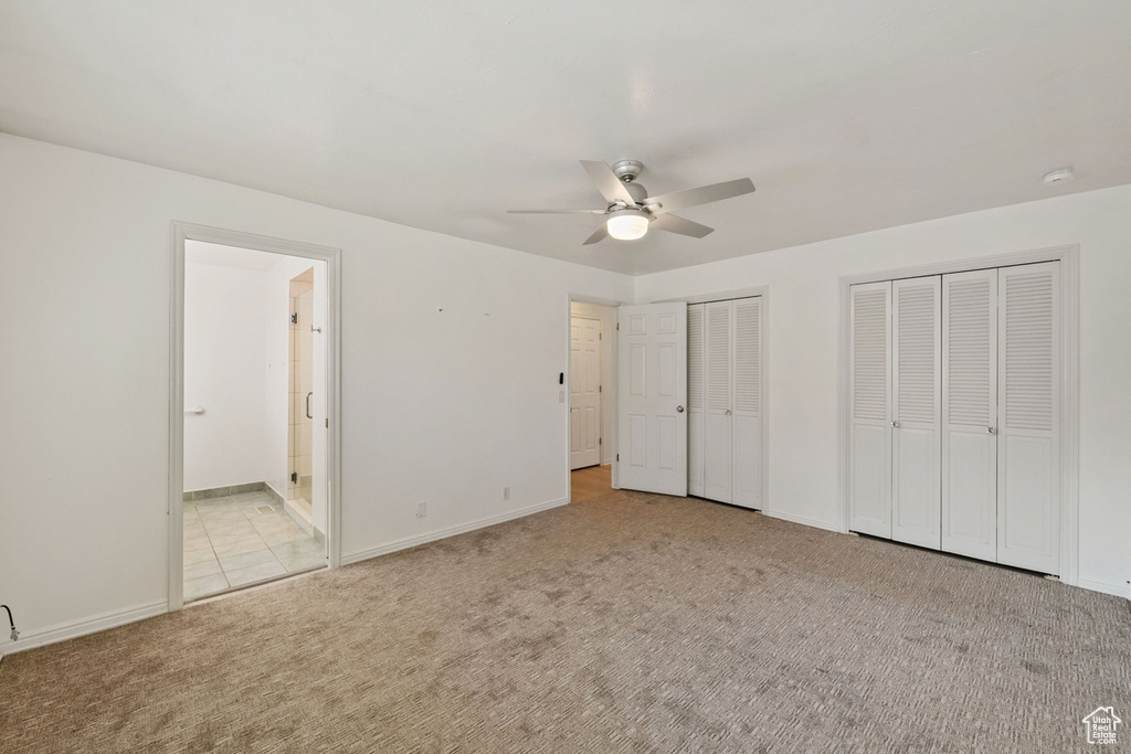 Unfurnished bedroom with multiple closets, ensuite bathroom, ceiling fan, and light colored carpet