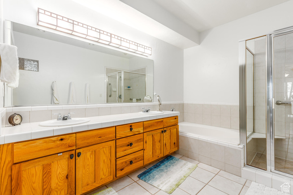 Bathroom featuring tile flooring, dual sinks, vanity with extensive cabinet space, and separate shower and tub