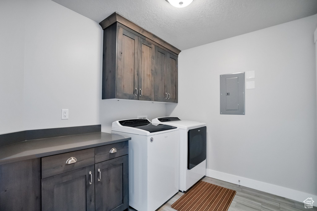 Laundry room featuring a textured ceiling, light wood-type flooring, cabinets, and washer and clothes dryer