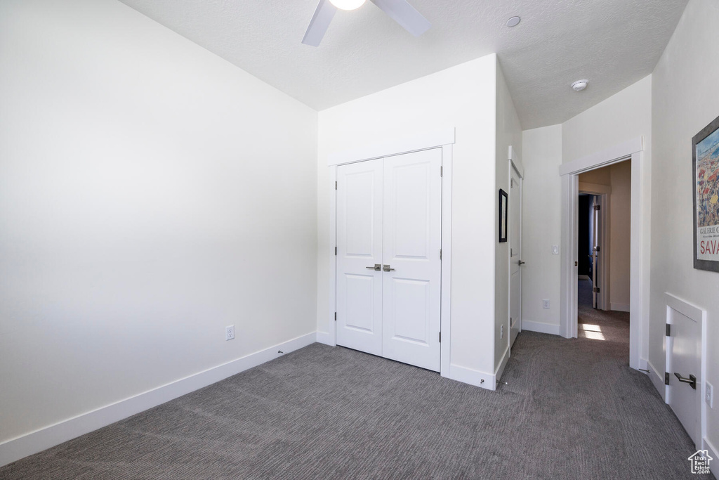 Unfurnished bedroom featuring dark colored carpet, ceiling fan, and a closet