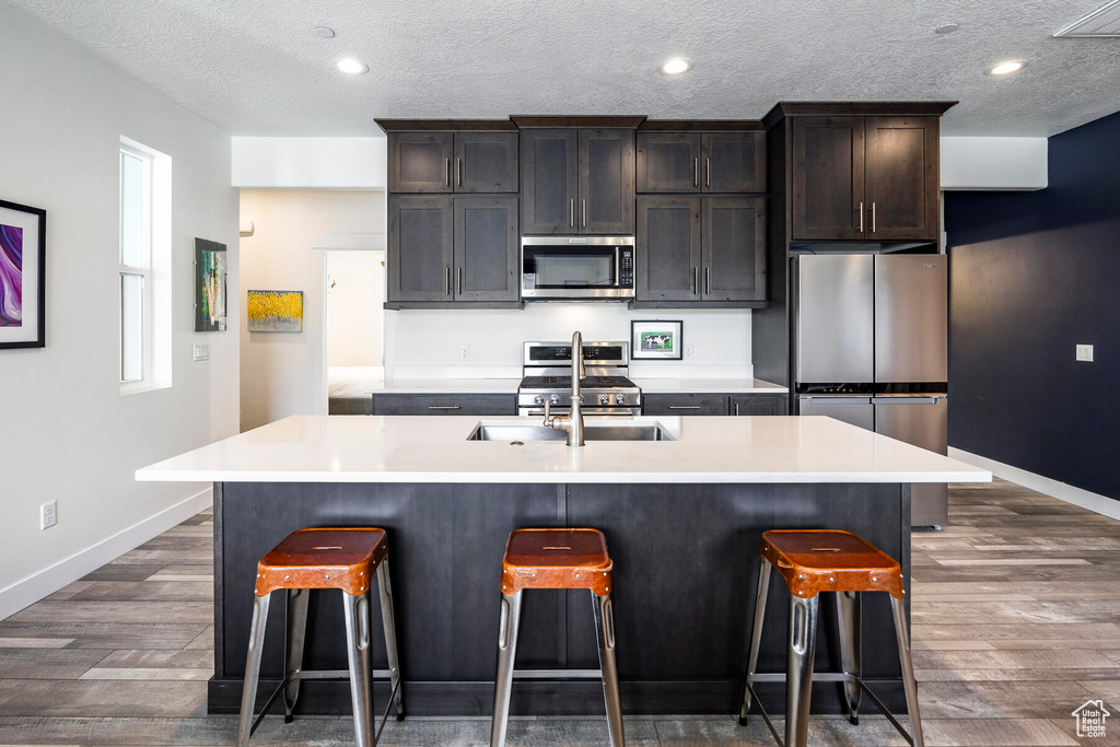 Kitchen featuring a kitchen island with sink, dark wood-type flooring, a breakfast bar, dark brown cabinets, and stainless steel appliances