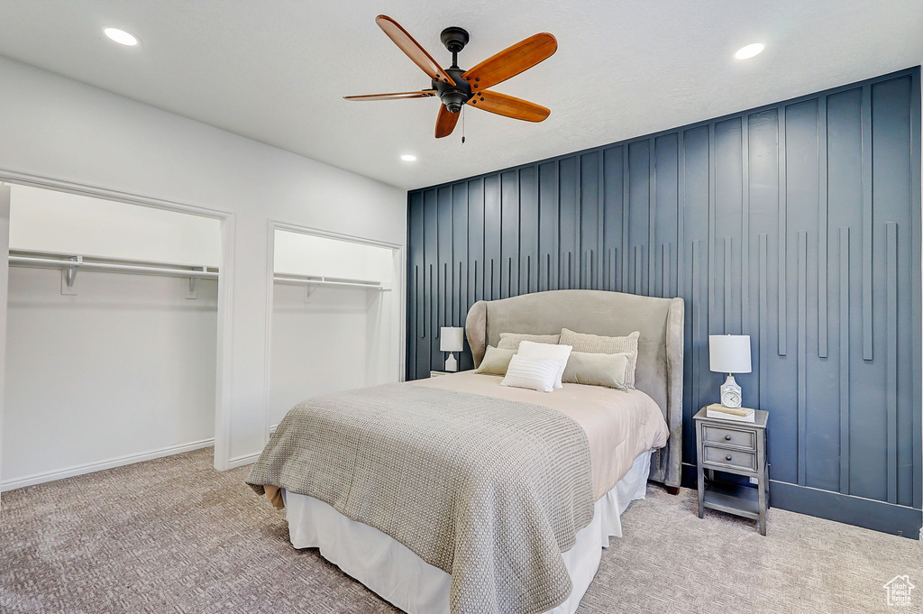 Bedroom featuring two closets, light carpet, and ceiling fan