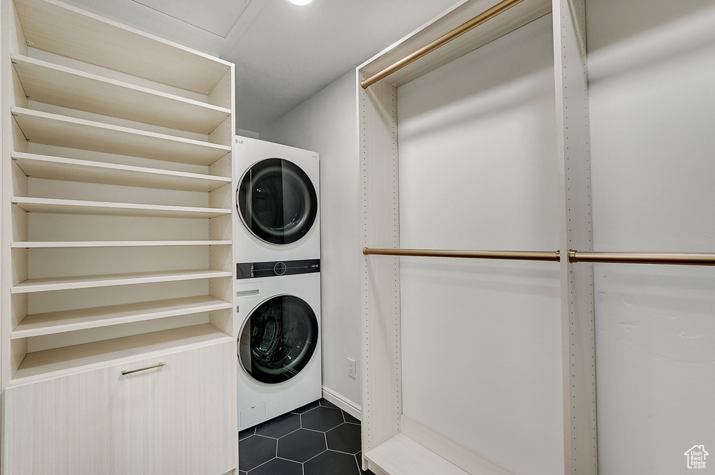 Laundry room with stacked washer and dryer and dark tile floors