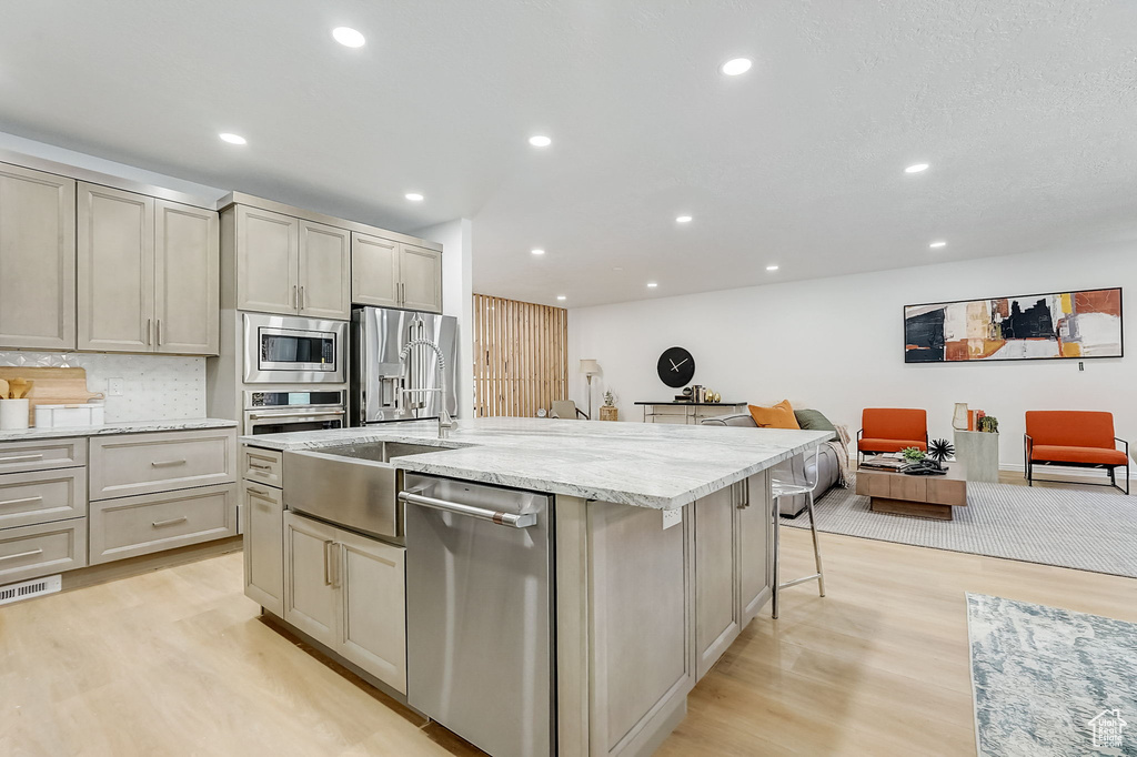 Kitchen with appliances with stainless steel finishes, a center island with sink, light stone counters, light hardwood / wood-style floors, and a kitchen breakfast bar