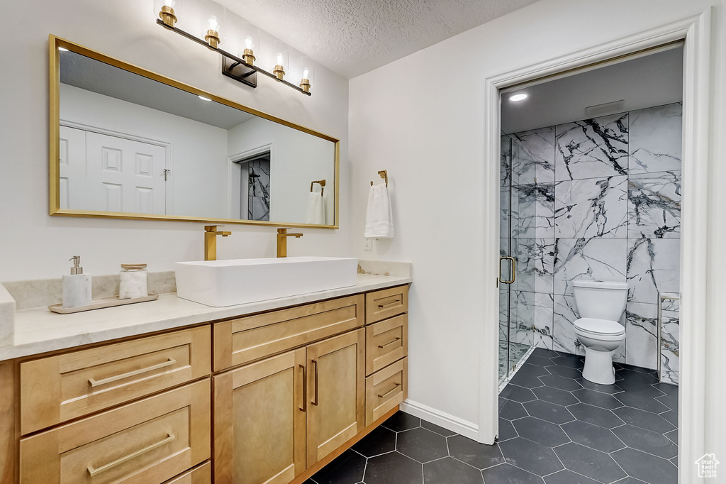 Bathroom with a textured ceiling, walk in shower, tile floors, oversized vanity, and toilet