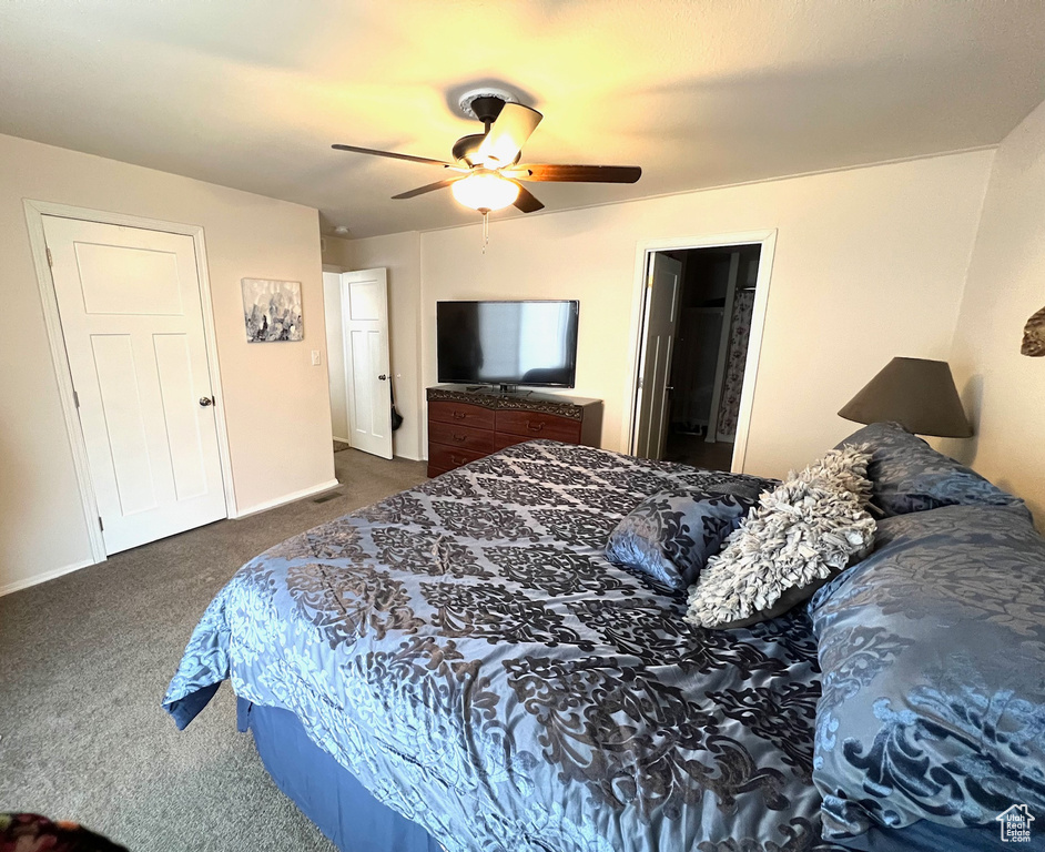 Bedroom with ceiling fan, dark carpet, and ensuite bathroom