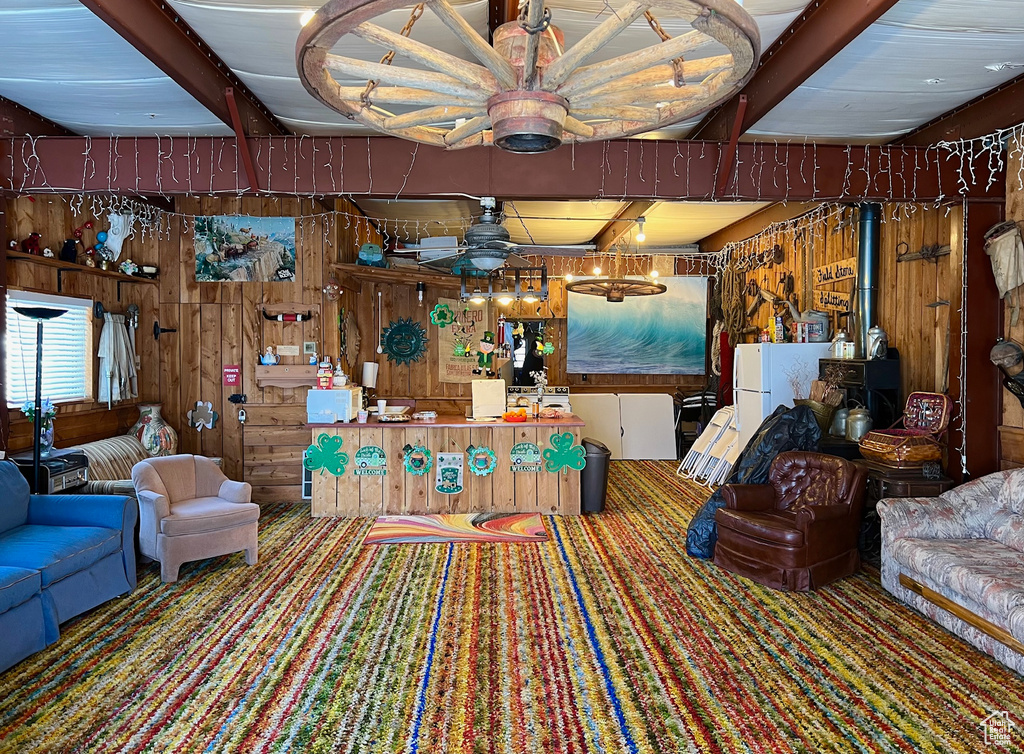 Carpeted living room with ceiling fan with notable chandelier, beamed ceiling, and wooden walls