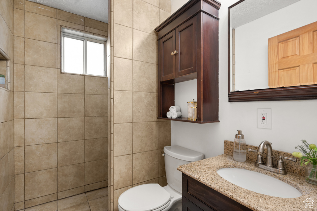 Bathroom with tile walls, a textured ceiling, toilet, and vanity