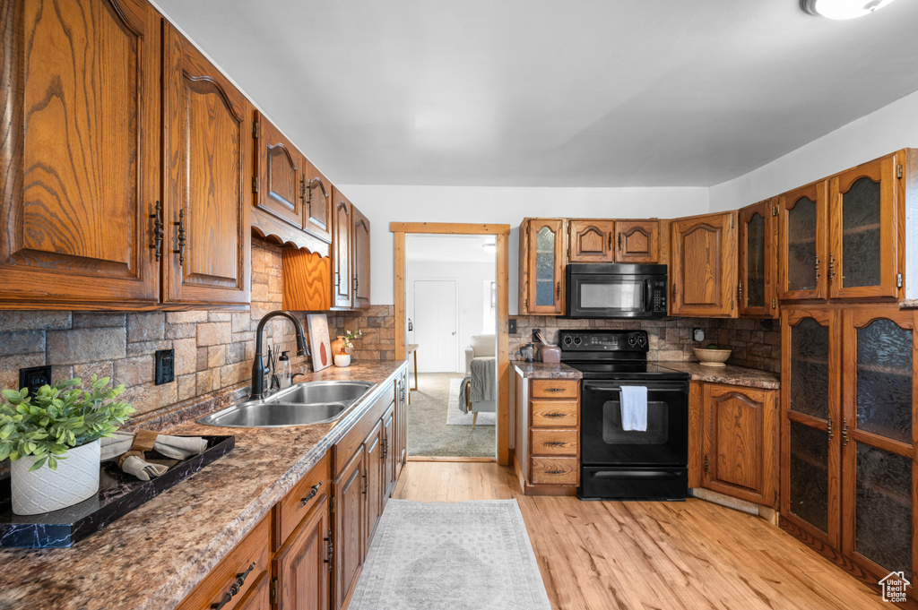 Kitchen featuring sink, tasteful backsplash, stone counters, black appliances, and light wood-type flooring