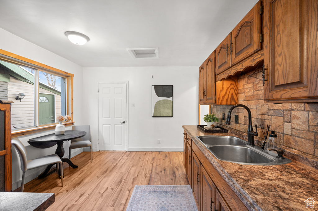 Kitchen with sink, light hardwood / wood-style flooring, tasteful backsplash, and dark stone counters