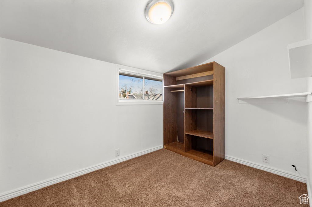Unfurnished bedroom with dark colored carpet and lofted ceiling