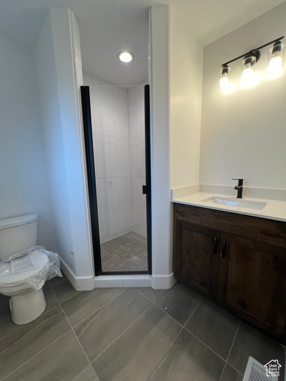 Bathroom featuring tile flooring, vanity, toilet, and a shower with shower door