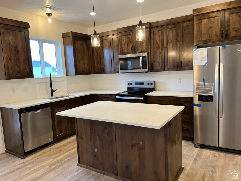 Kitchen featuring a center island, appliances with stainless steel finishes, light hardwood / wood-style floors, and dark brown cabinetry
